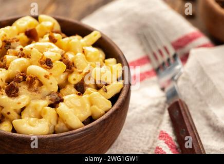 Großaufnahme von Makkaroni und Käse mit Speckstücken in einer Holzschale auf einem Tuch Stockfoto