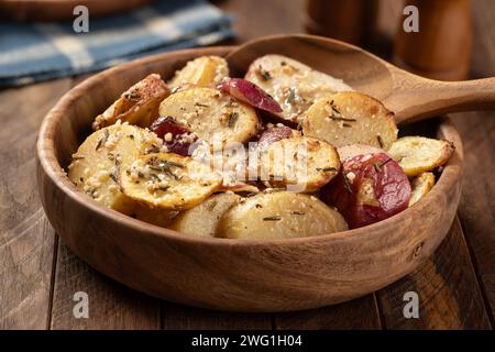 Gebratene Kartoffeln in Scheiben, gewürzt mit Rosmarin und Knoblauch in einer Holzschale auf einem rustikalen Tisch Stockfoto