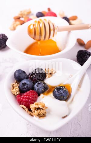 In der herzförmigen Schüssel Zutaten für ein gesundes Frühstück basierend auf: Normaler Joghurt, frischen Beeren, Honig und Mehrkornflocken Stockfoto