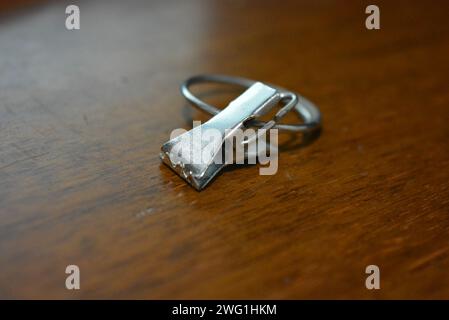 Eine kleine Metallkrabbe mit einem großen Ring wird zum Befestigen von Vorhängen verwendet und befindet sich auf einem Holztisch. Stockfoto