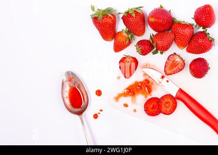 Reife und frische Erdbeeren, ganz und in Scheiben geschnitten auf weißem Hintergrund mit Messer und Löffel. Ansicht von oben. Stockfoto