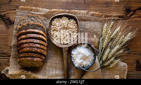 In Scheiben geschnittenes Vollkornbrot mit Getreide und verschiedenen Samen, Vollkornmehl, Gerstenkörner und Weizenohren auf Jutetuch. Ansicht von oben. Stockfoto