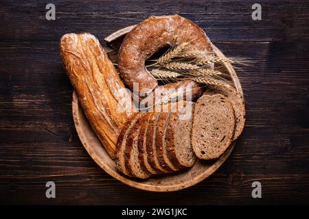 Auf dem Holzteller verschiedene Brotsorten, Vollkornbrot mit Samen und Getreide und ein paar Ähren Weizen. Stillleben. Ansicht von oben. Stockfoto