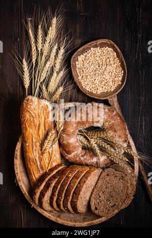 Auf dem rustikalen Holztisch, ein Holzteller mit verschiedenen Brotsorten, mit verschiedenen Samen und Müsli und ein paar Weizenohren. Stillleben. Blick von vorne Stockfoto