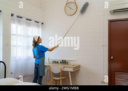 Die Haushälterinnen des Unternehmens, da sie sorgfältig Staubbürsten verwenden, um die Wände in einem Schlafzimmer zu reinigen und zu erfrischen Gründlichkeit und Engagement des Reinigungstees Stockfoto