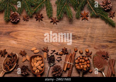 Blick von oben, auf einem strukturierten hölzernen Hintergrund, Kiefernzweige mit Tannenzapfen, verschiedene Gewürze und getrocknete Früchte. Leerzeichen für Ihren Text. Weihnachtsszene. Stockfoto