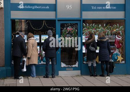 Menschen, die während der Weihnachtszeit über ein Schaufenster eines Immobilienmaklers Immobilien betrachten, Wimbledon Village, London SW19, England. Stockfoto