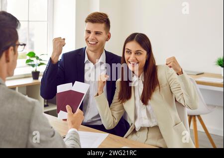 Glückliches Paar, das in einem Reisebüro sitzt und in den Urlaub geht und Pässe mit Tickets erhält Stockfoto