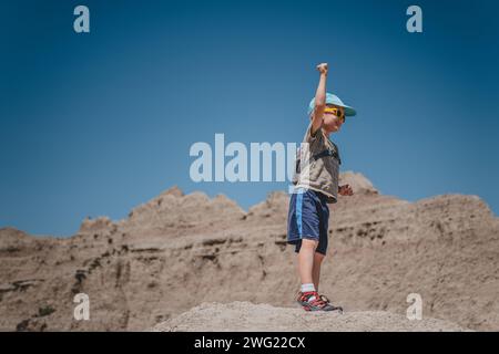 Ein kleiner Junge, der seine Hand auf einer Felsformation des Badlands-Nationalparks erhebt Stockfoto