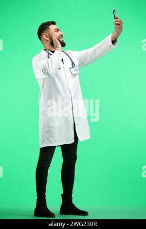 Der Doktor, in voller Höhe, auf grünem Hintergrund, spricht am Telefon Stockfoto
