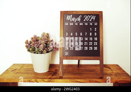 Monatskalender März 2024 und künstliche Pflanze auf hölzernem Hintergrund Stockfoto