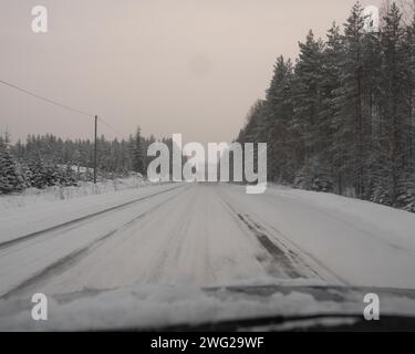 Eine vereiste und schneebedeckte Straße in Paltamo, Finnland im Winter. Die Straßenbedingungen sehen eisig und gefährlich aus. Stockfoto