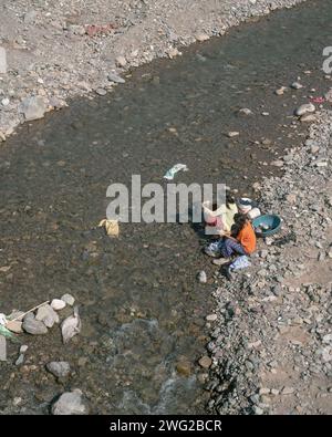 Zwei nepalesische Kinder waschen Kleidung im Fluss Mit Blick auf die Berge in Birendranagar, Provinz Karnali, West-Nepal. Stockfoto