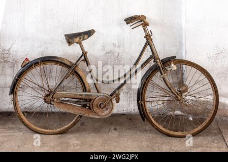 Staubiges, rostiges Fahrrad einer alten Frau, das sich gegen eine weiße Wand lehnt Stockfoto