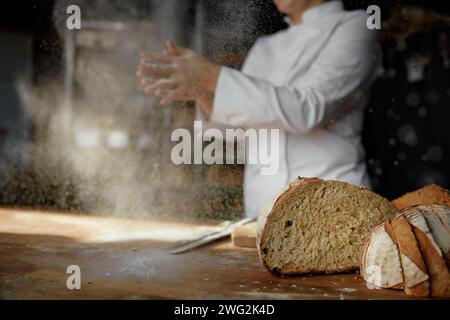 Weibliche Köcherhände klatschen in einer Wolke aus pulverförmigem Mehl über dem Tisch Stockfoto