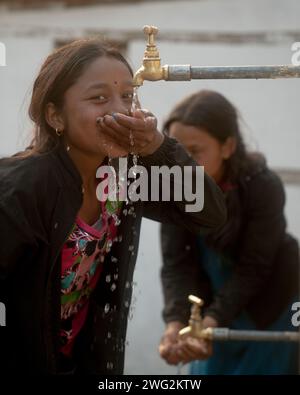 Ein junges nepalesisches Mädchen trinkt Wasser aus einer Dorfwasserquelle in Palata, Dolpa District, Westnepal, 2023. Stockfoto