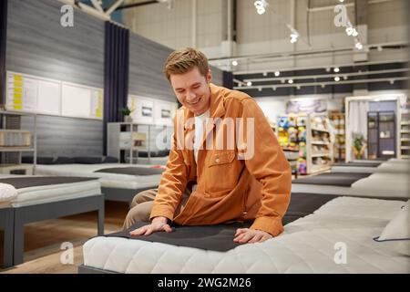 Gutaussehender männlicher Kunde, der auf einem neuen Bett im Möbelgeschäft sitzt Stockfoto