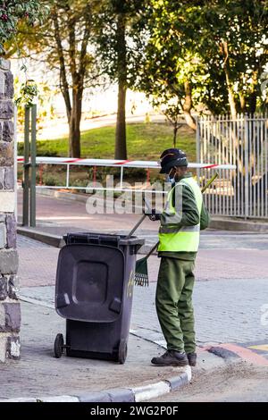 Schwarzer afrikanischer Mann, der Straßen fegt und aufräumt, Straßenreiniger in Overall und gut sichtbare Arbeitskleidung in Südafrika Stockfoto