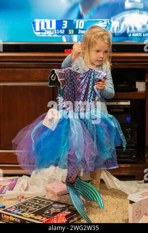 Ein dreijähriges blondes weißes Mädchen, das ein Meerjungfrauenkostüm hochhält, das sie als Geschenk erhalten hat. USA. Stockfoto