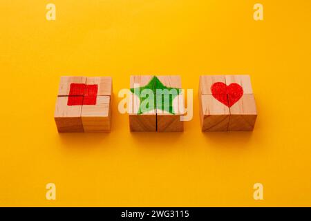Drei hölzerne Puzzleswürfel bilden ein Quadrat, einen Stern und ein Herz in der Mitte Stockfoto