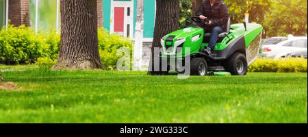 Gärtner fahren auf einem Rasenmäher Traktor fährt und mäht einen Rasen mit grünem Gras im Park. Stockfoto