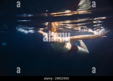 Ein hübscher junger Mann schwimmt im Urlaub in einem Swimmingpool unter Wasser. Stockfoto