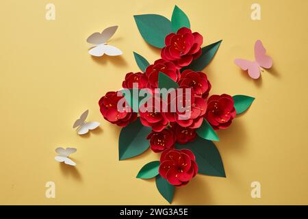Ein Haufen roter Papierblumen mit wenigen Schmetterlingen in vielen Farben. 3D-Papierblumen isoliert auf gelbem Hintergrund, dekorative Designelemente. Flache Lage, Stockfoto