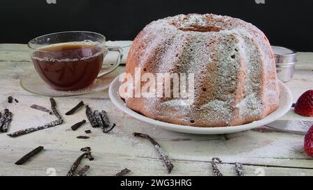 Altmodischer Sandkuchen mit einer Tasse schwarzem Tee und Vanillestücken auf hölzernem Hintergrund. Eidotter-Biskuitkuchen mit Straußbeeren auf rustikalem weiß Stockfoto