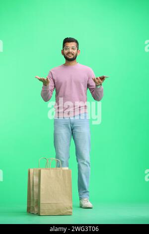 Ein Mann auf grünem Hintergrund, in voller Höhe, mit Taschen, spreizt seine Hände Stockfoto