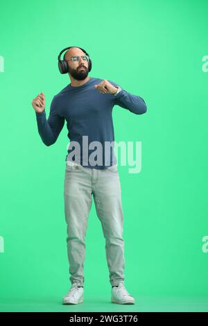 Ein Mann auf grünem Hintergrund, in voller Höhe, der Musik hört Stockfoto