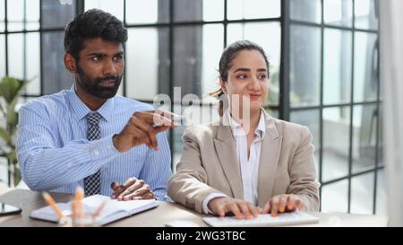 Junge indische Mentorentrainerin, die mit einer Kollegin spricht, die eine Trainee unterrichtet, und mit einer Arbeitskollegin ein Geschäftsgespräch führt Stockfoto