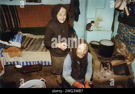 Vrancea County, Rumänien, ca. 1995. Zwei ältere Frauen in einem Landhaus, mit primitivem Küchenbereich und einem Bett am Ofen. Stockfoto