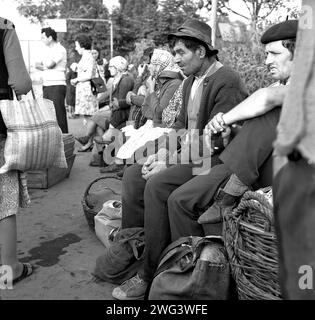 Die Sozialistische Republik Rumänien, ca. 1975. Stadtbewohner und Dorfbewohner, die Lebensmittel in Taschen und Körben transportieren, warten an einer Bushaltestelle in einer Stadt. Stockfoto