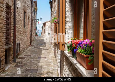 Blick auf die enge, typisch europäische Dorfstraße in der italienischen Stadt Frontone mit Sonne auf einer Seite zwischen Häusern und Gebäuden Stockfoto
