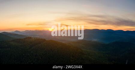 Luftaufnahme eines hellen nebligen Morgens über dunklen Hügeln mit Bergwaldbäumen bei Herbstsonnenaufgang. Wunderschöne Landschaft von wilden Wäldern bei Sonnenaufgang Stockfoto