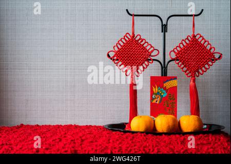 Ein roter Umschlag oder ang Pao (Worte bedeuten Drache und viel Glück) mit hängenden Anhängern und Orangen auf dem Tablett für das chinesische Neujahrskonzept. Stockfoto