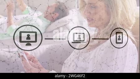 Digitale Symbole und kaukasische Frau, die ihr Smartphone zu Hause im Bett nutzt Stockfoto
