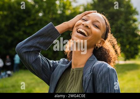 Junge Frau lacht draußen, drückt Glück aus, mit der Natur als Hintergrund. Stockfoto