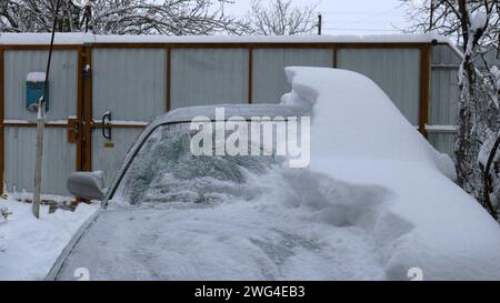 Teil eines grauen Autos, halb in einer dicken Schneeschicht begraben und halb von einer Schneewehung befreit, ein Personenwagen auf einem privaten Werft, der gerade frei wird Stockfoto