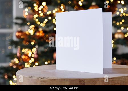 Leere quadratische Grußkarte, die vor einem unscharfen weihnachtsbaum mit Kopierraum steht. Zur Verwendung als Vorlage für Weihnachten und Hintergrund. Stockfoto