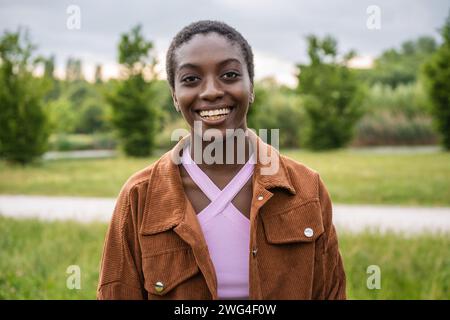 Junge afrikanische Frau lacht draußen, drückt Glück aus, mit der Natur als Hintergrund. Stockfoto
