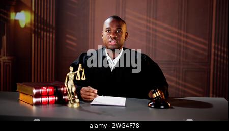 Selbstbewusster Reifer Männlicher Richter Schlägt Den Gavel Am Tisch Gegen Bücherregal Stockfoto