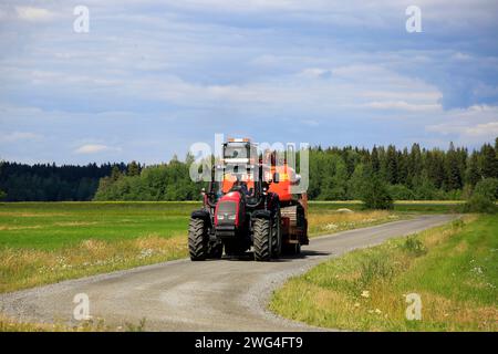 Jokioinen, Finnland - 13. Juli 2019: Der rote Valtra T151-Farmtraktor transportiert den Hitachi Zaxis 130 LCN-Bagger an sonnigen Sommertagen entlang der Landstraße. Stockfoto