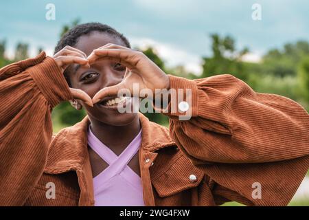 Ein junges Mädchen in der Natur, das Liebe mit einer Hand-Herz-Geste ausdrückt, Freude und Positivität ausstrahlt. Stockfoto