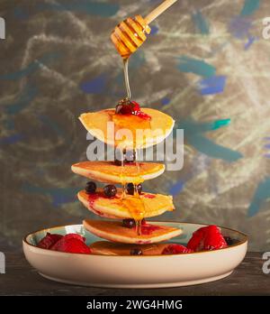 Fliegende Pfannkuchen mit gemischten Beeren und Honig, die darüber getränkt werden. Stockfoto