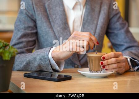Unerkennbare elegante Frau trinkt Kaffee in einem Café mit Smartphone auf dem Tisch Stockfoto