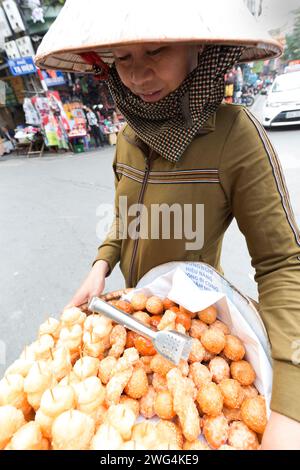 Vietnam, Hanoi, Straßenverkäufer, der umherläuft und süße Kuchen an Passanten verkauft. Stockfoto