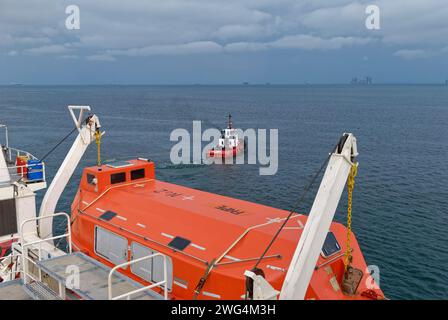 Ein Tug, der sich auf ein Schiff vorbereitet, das Port Gentil in Gabun abfährt, eingerahmt von den Hebezeugen der Life Boat Station auf der M/V Symphony. Stockfoto