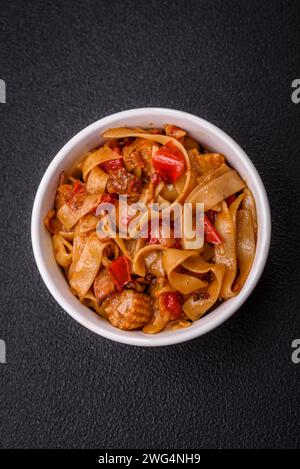 Köstliches asiatisches udon-Gericht mit Gemüse, Pilzen, Salz und Gewürzen auf einer Keramikplatte auf dunklem Betonhintergrund Stockfoto