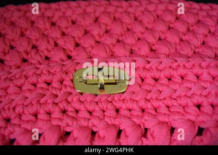 Auf einer schwarzen Hochglanzbaa eine Reflexion.ckground ist eine rosa gewebte Damentasche auf der Schulter mit einem goldenen Babybett und einem Dosenöffner und einer Reflexion. Stockfoto